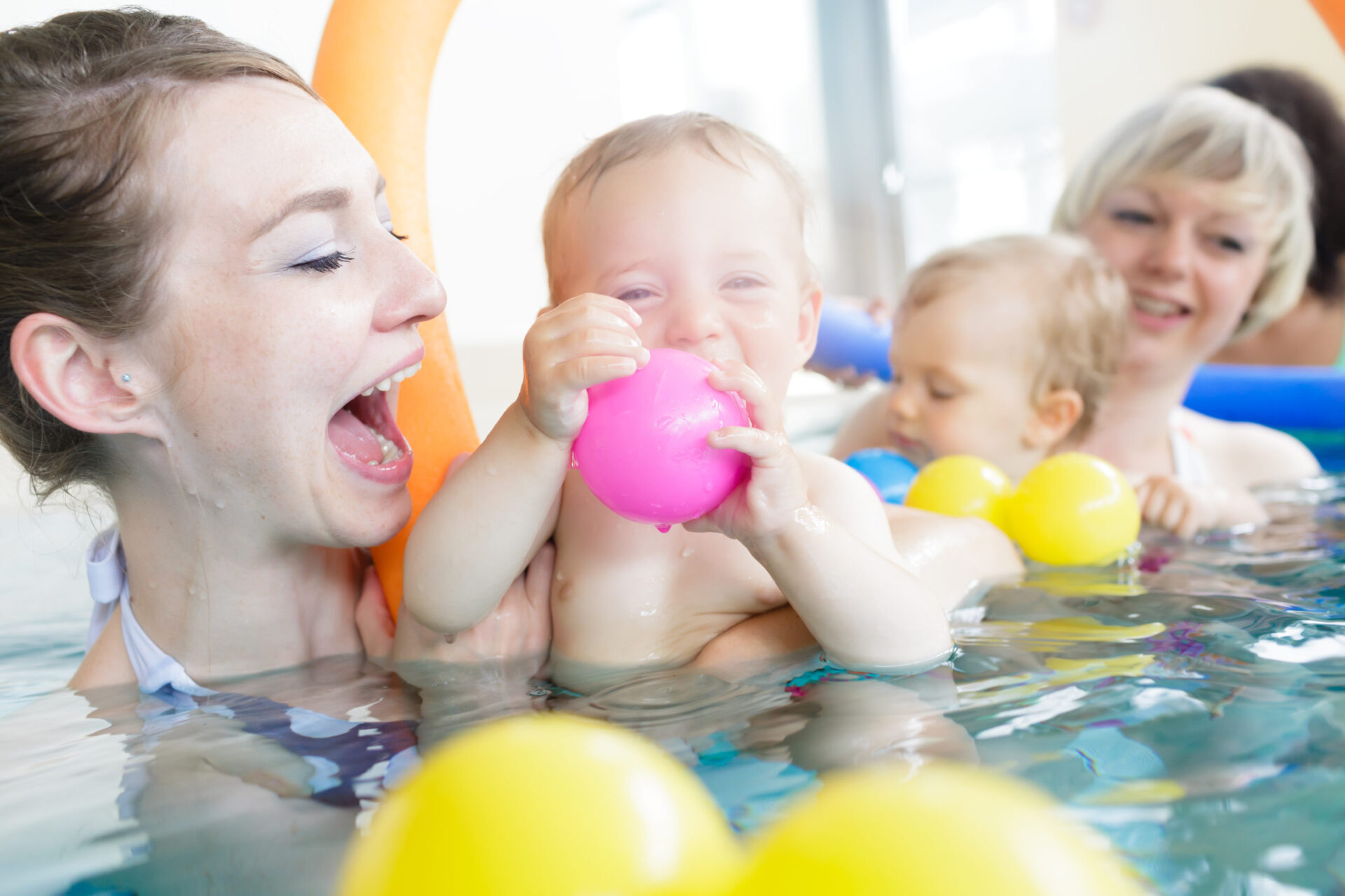 Mothers and their kids having fun at baby swimming lesson between lots of water balls