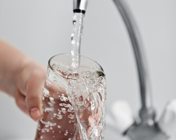 Human hand holding glass pouring fresh drink water at kitchen faucet
