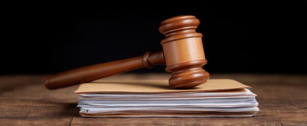 A polished judges gavel lies atop a thick stack of official legal documents